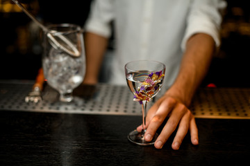 Professional bartender serving a cocktail in the glass decorated with flowers