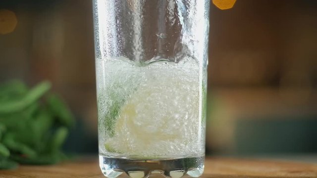 sparkling clear water is poured into a tall glass tumbler with slices of fresh lime on the bottom. A lot of bubbles go up. The camera moves up. pieces of fruit float.