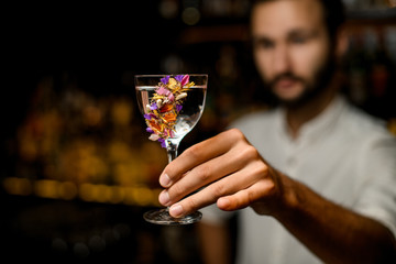 Attractive bartender serving a cocktail in the glass decorated with flowers