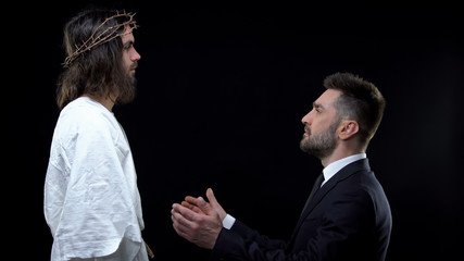 Male businessman kneeling down front of Jesus praising God, asking forgiveness