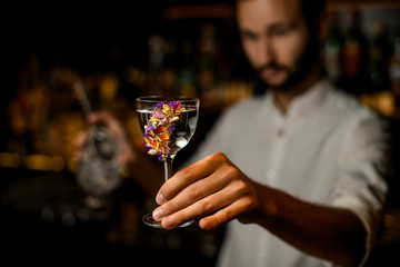 Attractive blurred bartender serving a cocktail in the glass decorated with flowers