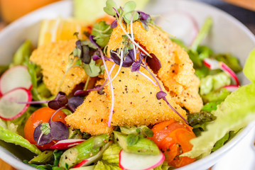 A plate of Crispy Calamari Salad with lettuce, radish, lemon, tomatoes, asparagus  and avocado.