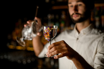 Attractive bartender serving a cocktail in the glass decorated with beautiful flowers