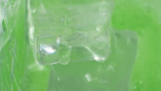 green cocktail is poured into a glass. there are cubes of cold ice. The drink drips and bubbles and splashes. macro mode. Angle from above. the beginning of a fun party. studio lighting.