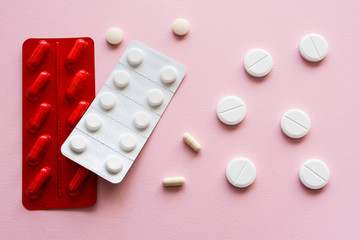 Medicine capsules and tablets  in red and white blister packs on a pink background. Isolated. Copy space.