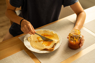 Woman adding apricots jam on homemade pancakes in the morning.