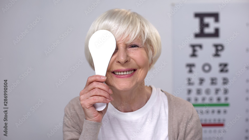 Wall mural Retired female closing eye and smiling to camera, successful cataract surgery