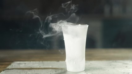 a frosted glass of vodka sits empty on a frozen glass tray. steam slowly escapes from it. Party concept. Large drops on the glass. - Powered by Adobe