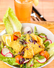 A plate of Crispy Calamari Salad with lettuce, radish, lemon, tomatoes, asparagus  and avocado.