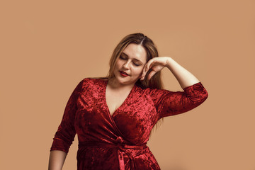 Enjoying my beauty. Plus size young woman in velour dress touching her face and keeping eyes closed while standing in studio