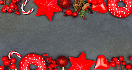 Red and black Christmas composition. Red holly berries, glass baubles and Xmas decor on dark...