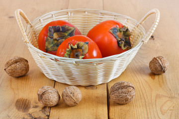 Autumn fruits. Persimmons in a wicker basket on a wooden board on a wooden background. Nuts