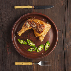 Appetizing chicken legs served in a wooden plate with green chili peppers. Top view