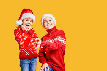 Happy boy in Santa hat giving Christmas gift box to excited girl in red sweater with deer on yellow background