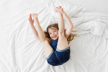 Smiling young girl bouncing on her back on a bed