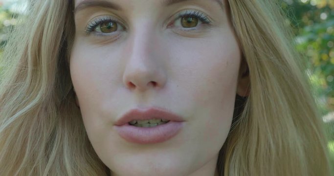 Close up of an attractive young woman with blonde hair, talking confidently to the camera