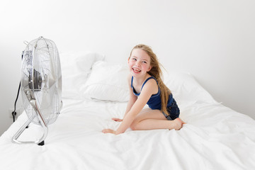 Happy little girl on bed facing a fan