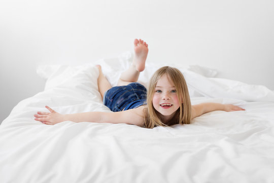 Smiling young girl lying on bed with arms extended