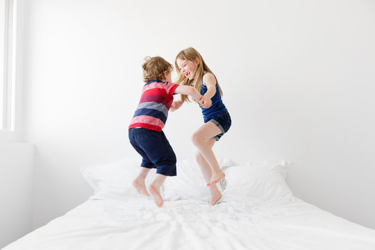 Brother and sister jumping and dancing on bed together