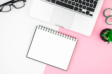 Blank notepad and silver laptop top view on female office table with pop pink and white background. Beauty blogger concept mockup