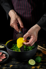 Cooking fresh diet keto salad with beef meat, arugula, fruits and nuts by chef hands on black table background.