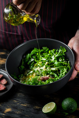 Cooking fresh diet keto salad with beef meat, arugula, fruits and nuts by chef hands on black table background.