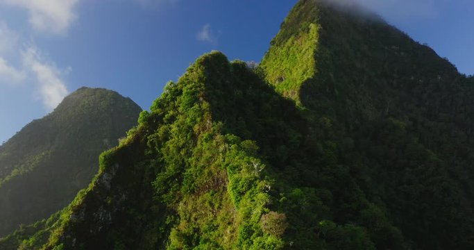 Aerial drone shot pushing in on lush green island mountain peaks, flying over green mountain ridges, gorgeous island landscape