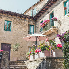 Fototapeta na wymiar View of a street of San Marino. Flowers on the windows. Blooming petunias in pots, as a decoration of the facade of the house. Grow flowers on the street.
