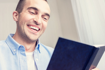 Young attractive guy resting at home and reading a book, man smiling, portrait, close up, toned