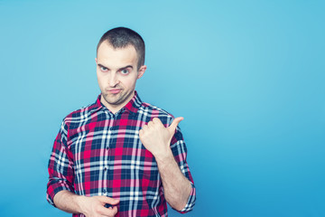 Young attractive manager in everyday clothes, man points to the empty space, looking at camera, portrait, front view, blue background, copy space, advertising, slogan, toned