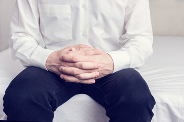 Man sits quietly on the bed with his hands folded, man's hands, cropped image, close up, toned