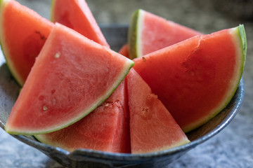 Fresh watermelon sliced in grey handmade pot on granite platform in kitchen.