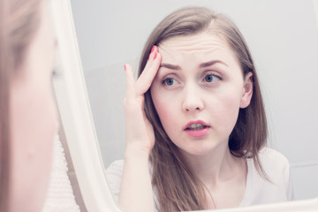 Sleepy young woman, reflection in the mirror, girl is upset because of the first wrinkles looks in the mirror, close up, toned