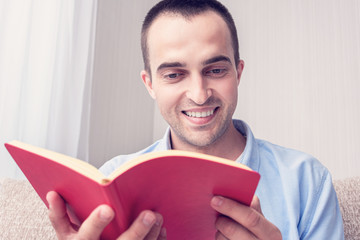 Young man sitting at home, guy reading a book, portrait, close up, toned