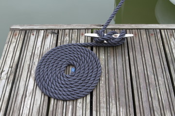 The mooring dark blue rope of a boat, coiled on a bollard, with the end neatly folded beside it. Wooden pier on the lake on a summer day.