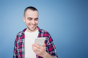 Attractive man smiling and reads sms on his smartphone, front view, blue background, copy space