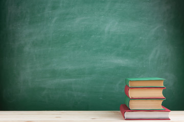 Education and reading concept - group of colorful books on the wooden table in the classroom, blackboard background