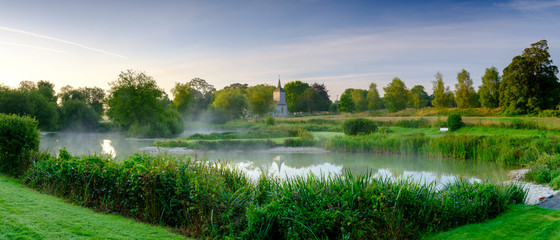 Misty dawn light on Stoke Charity village pond and St Michael's Church, Hampshire, UK