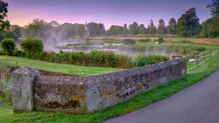 Misty dawn light on Stoke Charity village pond and St Michael's Church, Hampshire, UK