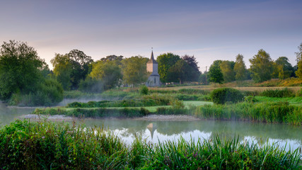 Misty dawn light on Stoke Charity village pond and St Michael's Church, Hampshire, UK