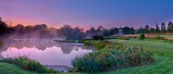 Misty dawn light on Stoke Charity village pond and St Michael's Church, Hampshire, UK