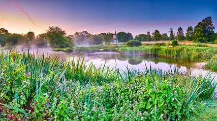 Misty dawn light on Stoke Charity village pond and St Michael's Church, Hampshire, UK