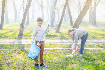 Young boy picking up trash in the park. Volunteer and ecology concept