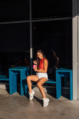 Fototapeta na wymiar Stylish happy young brunette woman wearing white shorts and sneakers holding pink cup of coffee to go.