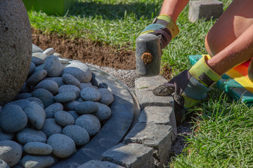 Parts of a hobby worker with work gloves arranging basalt cobblestones into the curb of a garden fountain