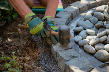 Parts of a hobby worker with work gloves arranging basalt cobblestones into the curb of a garden fountain