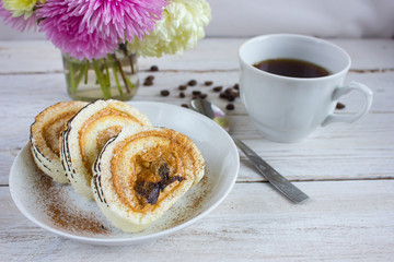 Cup of coffee on a white wooden table, a cake and a bouquet of pink flowers