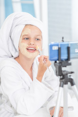 Young girl in towel on her head  filming the video for her followers about clay facial mask . Kids blogger concept