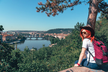 Young female tourist in a cowboy hat with sunglasses and a backpack, enjoying great view on the old town of Prague. Praha, Travel tour to Europe. copy space for text