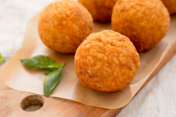 Homemade fried Arancini with basil on a rustic wooden board, side view. Italian rice balls. Closeup.